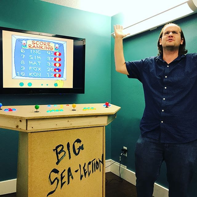 Thomas stands beside the custom MAME cabinet his team built for Ship It Day